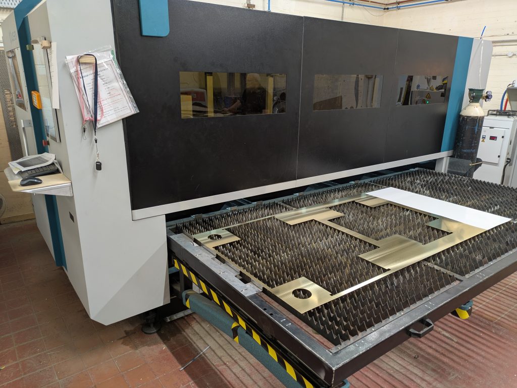 CNC laser machine cutting brushed brass sheet – brass parts on pull-out bed.