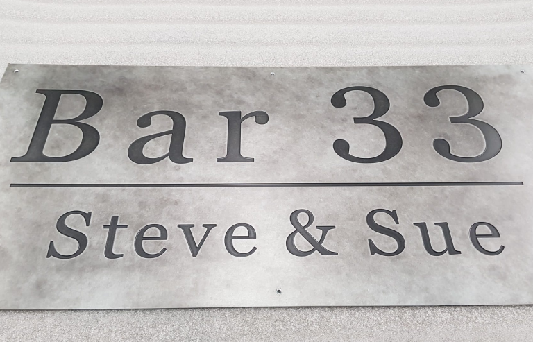 CNC engraving on sheet metal example an engraved Bar 33 sign in patinated zinc with serif lettering, featuring the names Steve & Sue.