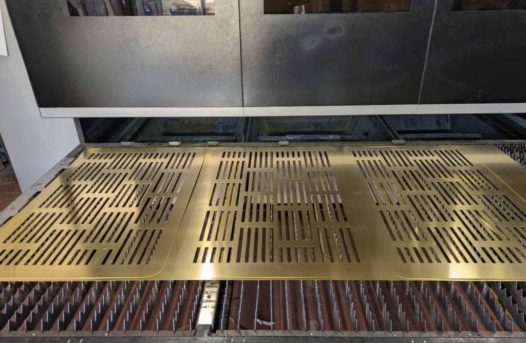 Laser cutting machine producing precision brass panels with decorative slot patterns at MS Laser Services.